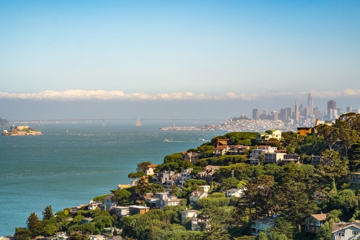 View of a city skyline and island across a bay with hills and houses in the foreground.