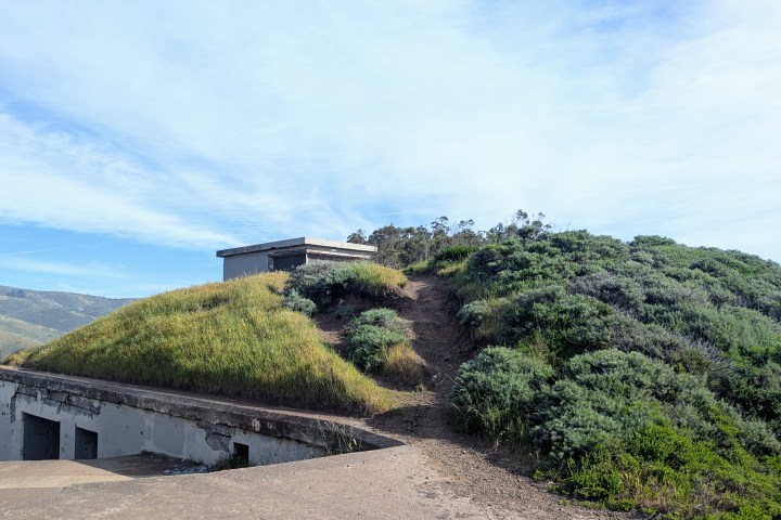 Grassy hill with a small structure and path under a blue sky.