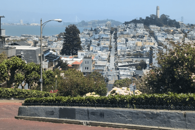 View of a hilly city street with distant bay and bridge in the background.