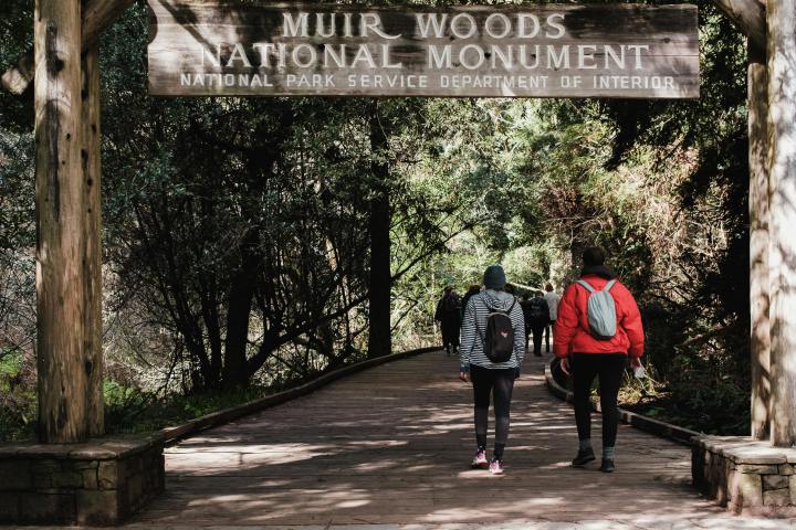 Two people walking under Muir Woods National Monument entrance sign.