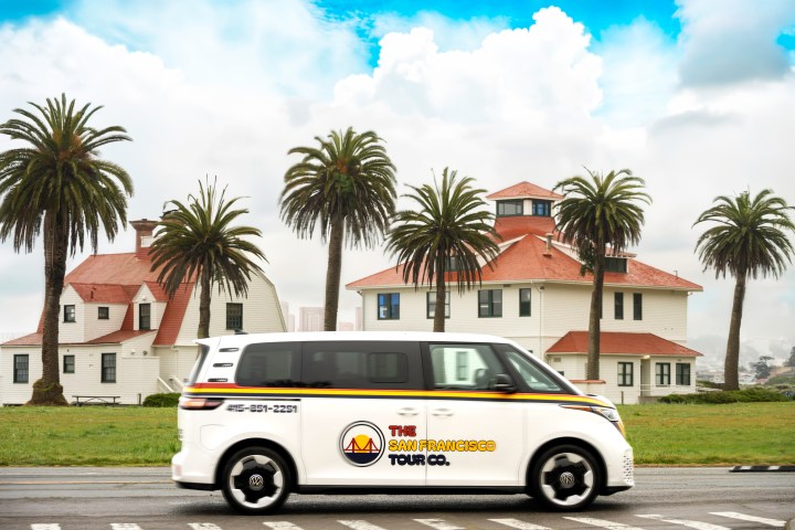Van with tour company logo driving past palm trees and white buildings.